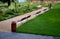 Park benches lined with wood along the entire wide threshing gravel beige path, lawns, flower lush, perennial flower beds blooming