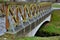 A park bridge with a wooden railing leads across a stream. in the nature park there is an arched concrete bridge and a maze of hor