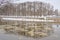 Park covered in snow with bare trees reflecting in the water of Emajogi river