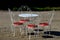 Park seating at a patisserie made of white painted wires bent into a shell shape. red leather cushions. chairs and tables on the s