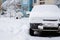 Parked car covered with snow - snow storm, car after a heavy snowfall, a lot of snow on the car, car in the snowy yard, front view