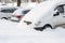 Parked cars, covered in snow, stand along the road. Snowfall in the city, falling snowflakes. Concept: traffic collapse, increased