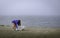 The parking attendant collects garbage in the beach parking lot in the foggy morning.