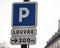 Parking road sign and signpost from the distance to the Louvre in Paris