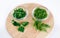 Parsley and dill leaves in two glass bowls and lone twigs on round wooden cutting board view from above