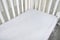 Part of baby cot, close up. Mattress and sheets in white crib.