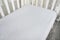 Part of baby cot, close up. Mattress and sheets in white crib.