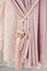 Part of beautifully draped curtain on the window in the room. Floral tassel tieback. Close up of piled curtain. Pink luxury
