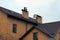 Part of a brown brick private house with windows under a tiled roof and two chimneys