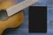 Part of a brown guitar and a vertical screen of a black tablet on a blue wooden surface. The concept of a mock up for advertising