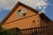 Part of the brown house behind the fence with a window in the attic and a satellite dish on the wall