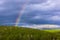 Part of colored rainbow on dark thunder clouds with green forest mountain background. horizontal view.