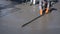 Part of construction worker with rubber glove using long triangle trowel to spread and plastering cement on the floor in