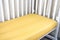 Part of cot, close up. Mattress and yellow sheet in white bed.