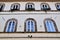 Part of the facade, in the shade, with 8 large white arched windows of a historic building in Lucca.