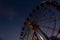 Part of a ferris wheel with lights of night illumination on a background a dark blue sky. Amusement park in Spain in the evening.