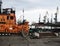 Part of a fire orange towing vessel against the background of a tanker and a port crane and a train with coal