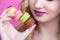 Part of the girl face with a stack of multi-colored macaroons in her hand near lips on a pink studio background, the concept of