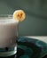 Part of a glass of banana cocktail on a green plate with a slice of banana