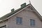 Part of a gray brick house with windows under a green tiled roof