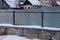 Part of a gray metal fence on a concrete foundation overgrown with gray dry vegetation in white snow