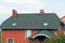 Part of the house with a green tiled roof and a red brick wall with windows