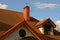 Part of the house with windows in the attic with brown tiles and pipe