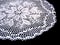 A part of isolated crocheted white doily with a pattern of flowers on a black background. Round decorative doily
