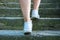 Part of the legs of a woman in white sneakers walking along stone steps.