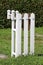 Part of newly made white wooden picket fence with mounted brown metal mailbox surrounded with uncut grass and dark green hedge