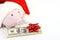 Part of piggy bank with Santa Claus hat and stack of money american hundred dollar bills with red bow