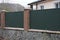 part of a private wall of a fence made of green metal and brown bricks