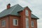 Part of a red brick house with windows under a green tiled roof