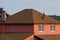 Part of a red house with windows with a brown tiled roof