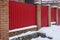 Part of a red metal brick fence and a closed door in white snow