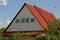 Part of a rural house from the attic with a window under the red slate against the sky