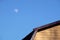 Part of rural house wall covered with yellow siding and brown metal roof and round moon in the sky front view