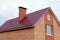 Part of a two-story private building of red brick against a clear sky. Fragment of a roof with a pipe and a window on the house.