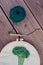 Part view of embroidery project in a hoop together with punch needle and green ball of cotton yarn on wooden ribby planks. Punch