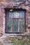 Part of the wall of an abandoned red brick house with a window. Trees grow inside.