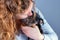 Part of a woman with brown curls, she lovingly kisses a tiny Jack Russel Terrier puppy in her arms