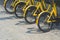 Part of of yellow bikes parked on cobblestone pavement in public area