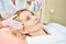 Partial female beautician doing laser depilation of forehead of smiling woman