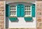 Partial front exterior of white cottage with teal shutters and window boxes with red and white impatiens