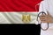 Partial photograph of a doctor with a stethoscope in a professional medical uniform against the background of the national flag of