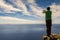 Partial silhouette of a man taking picture on his smart phone standing on a top of a mountain. Warm sunny day. Blue sky and vast