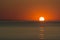 Partial sunrise from the sea, with the sun on right, orange sky and low reflection on the surface of water