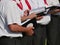 Partial view of 3 singers of a choir, holding in their hands textbooks, dark trousers, white short-sleeved shirt, red kerchief