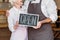 partial view of coffee shop owners in aprons holding open chalkboard together