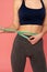 Partial view of european woman measuring waist. Studio shot of fit girl with measure tape posing on pink background.